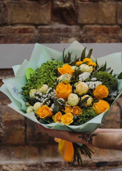 side view of bouquet of yellow color roses white color peonies eustomas and trachelium background flowers on brick wall background